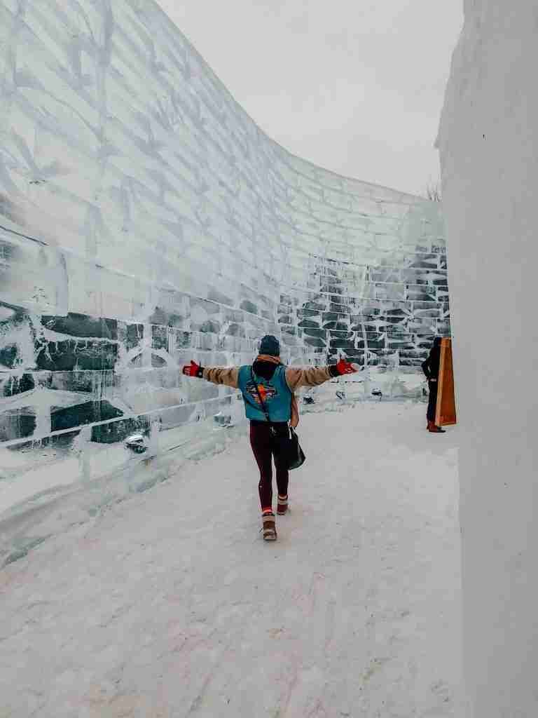 A girl runs down an icy corridor with tall icy walls of the Ice Castle at the Carnaval de Quebec surrounding her