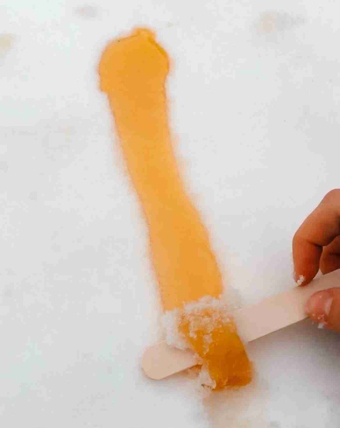 maple taffy poured on to the snow as someone rolls it using a popsicle stick