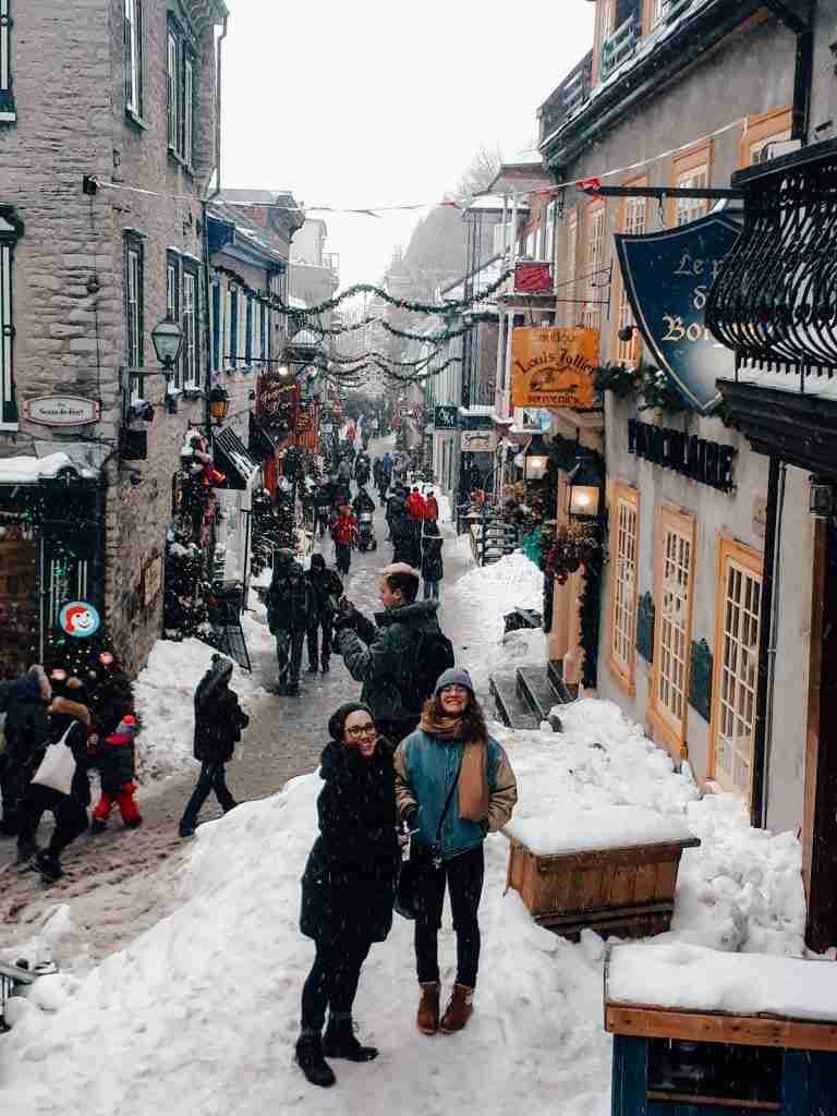 2 girls stand on top of snow in the decorated streets of Quebec city