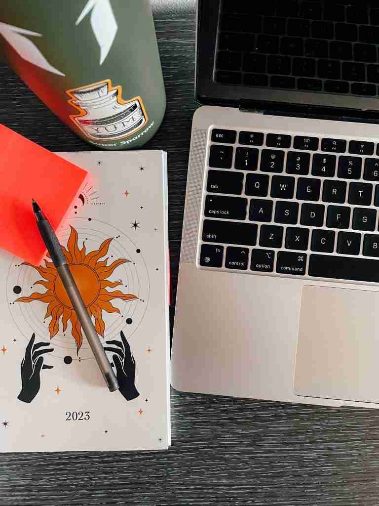 A daily planner, sticky note, lap top, pen and water bottle sitting on someones workspace