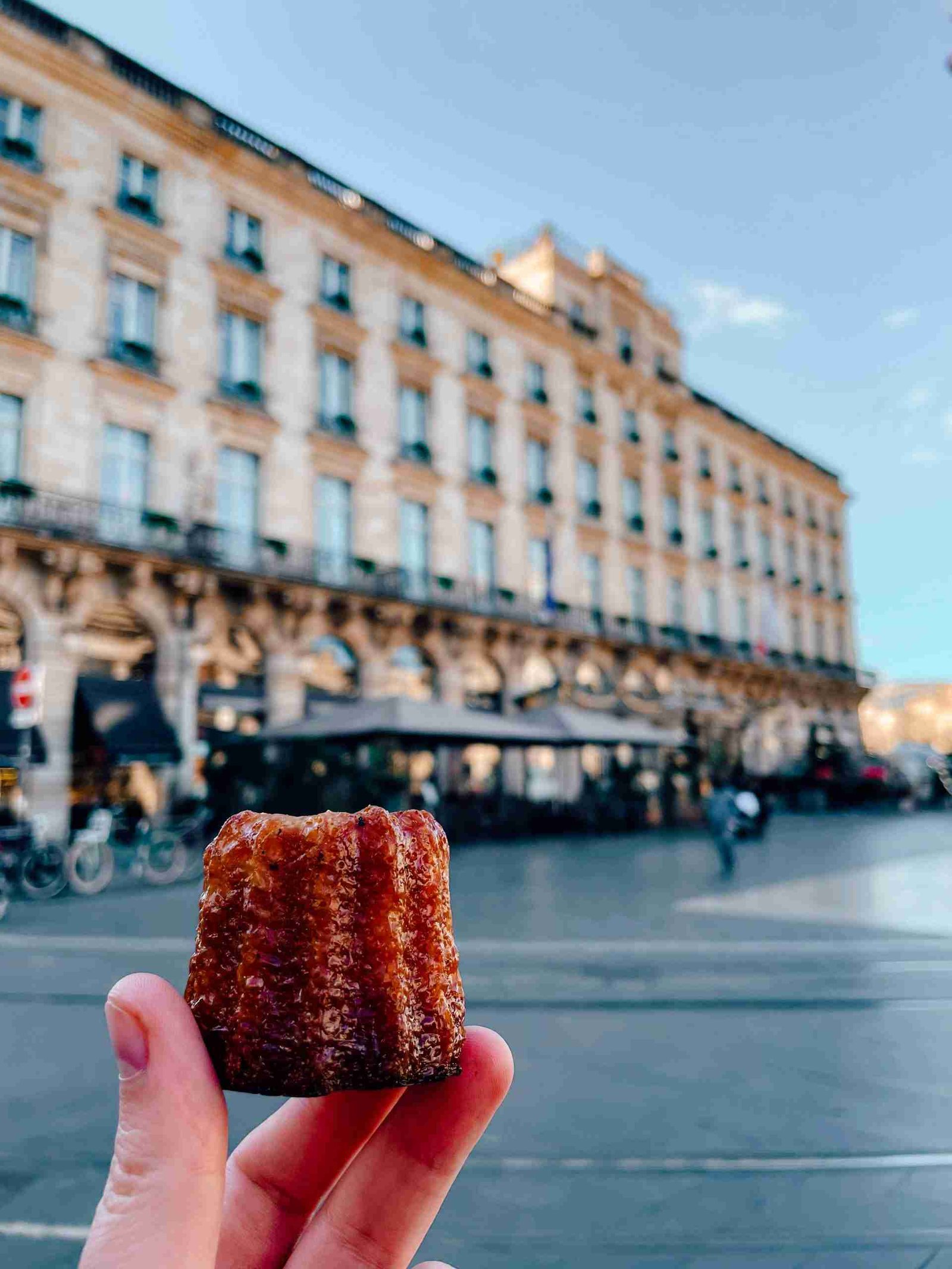 someone holding a canalé in front of the place de la comedie in Bordeaux - one of the best things to do in Bordeaux