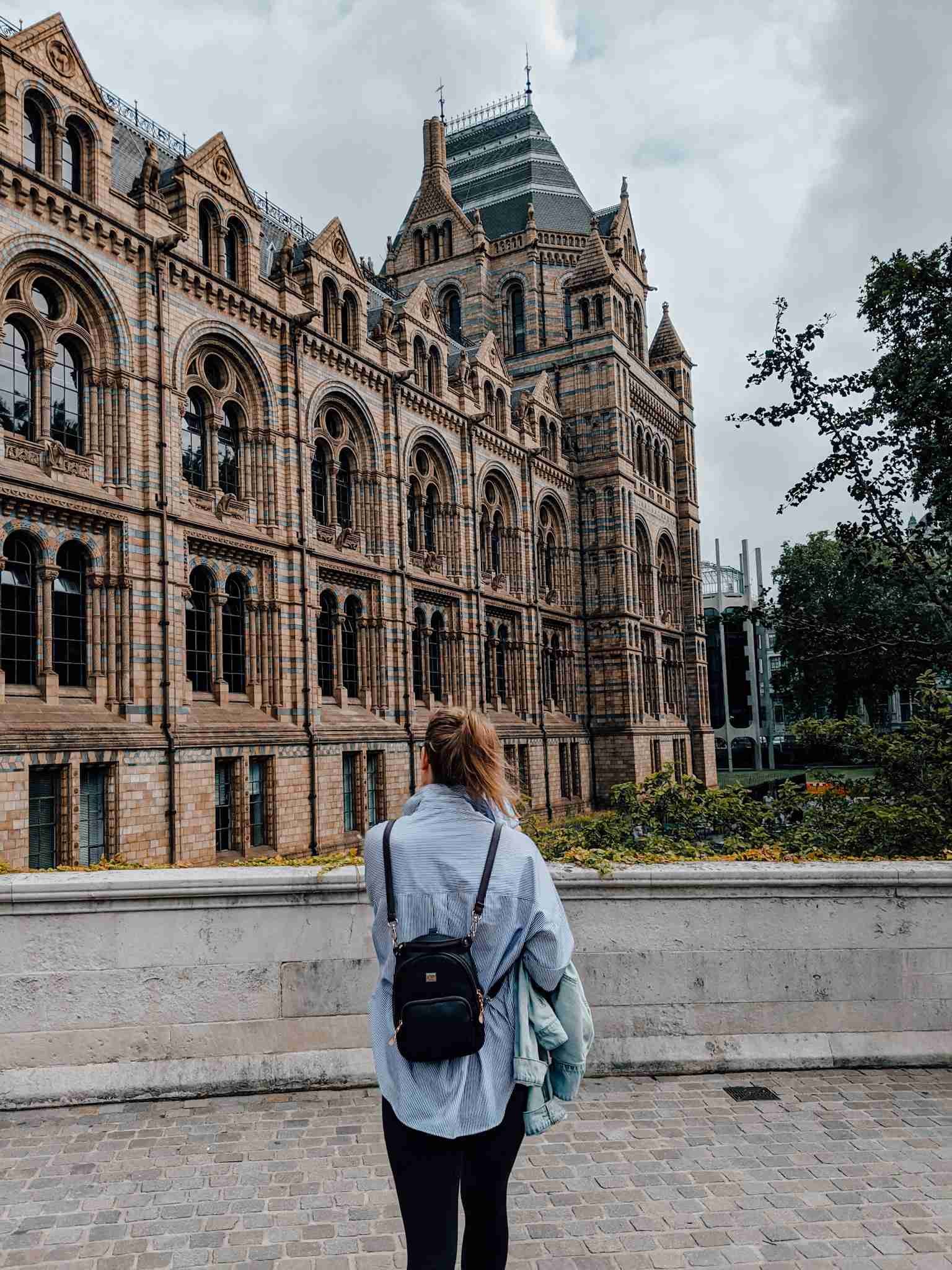 A girl walking towards the exterior of the Natural History Museum in London - one of London's museums.