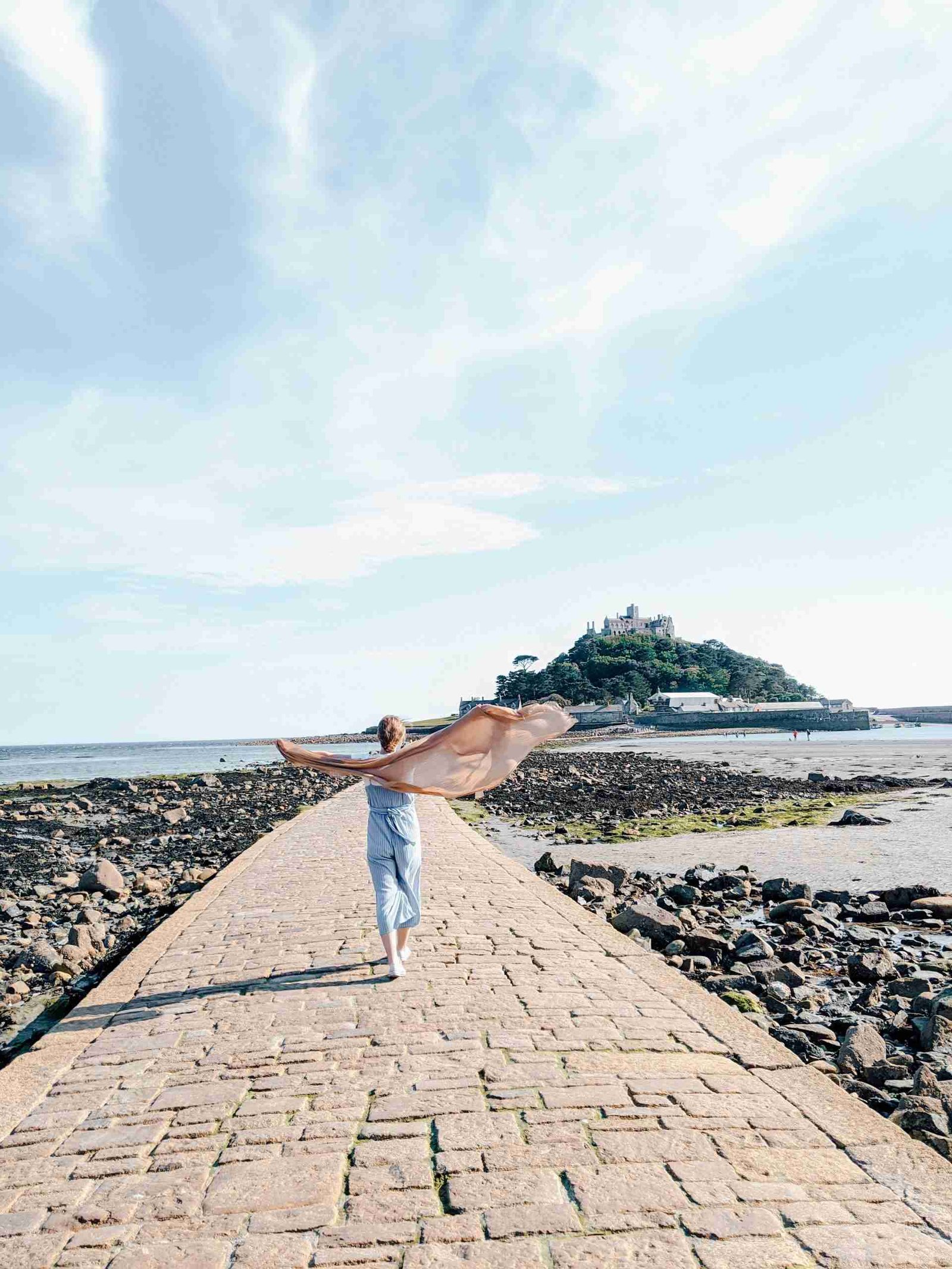A girl walking towards the wind in St. Michaels Mount in Cornwall, her scarf blowing behind her.