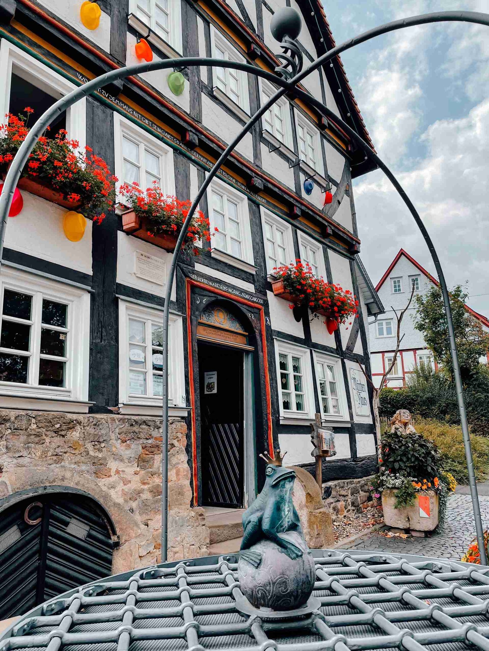 A mini frog prince statue in Alsfeld with a timber framed house behind it