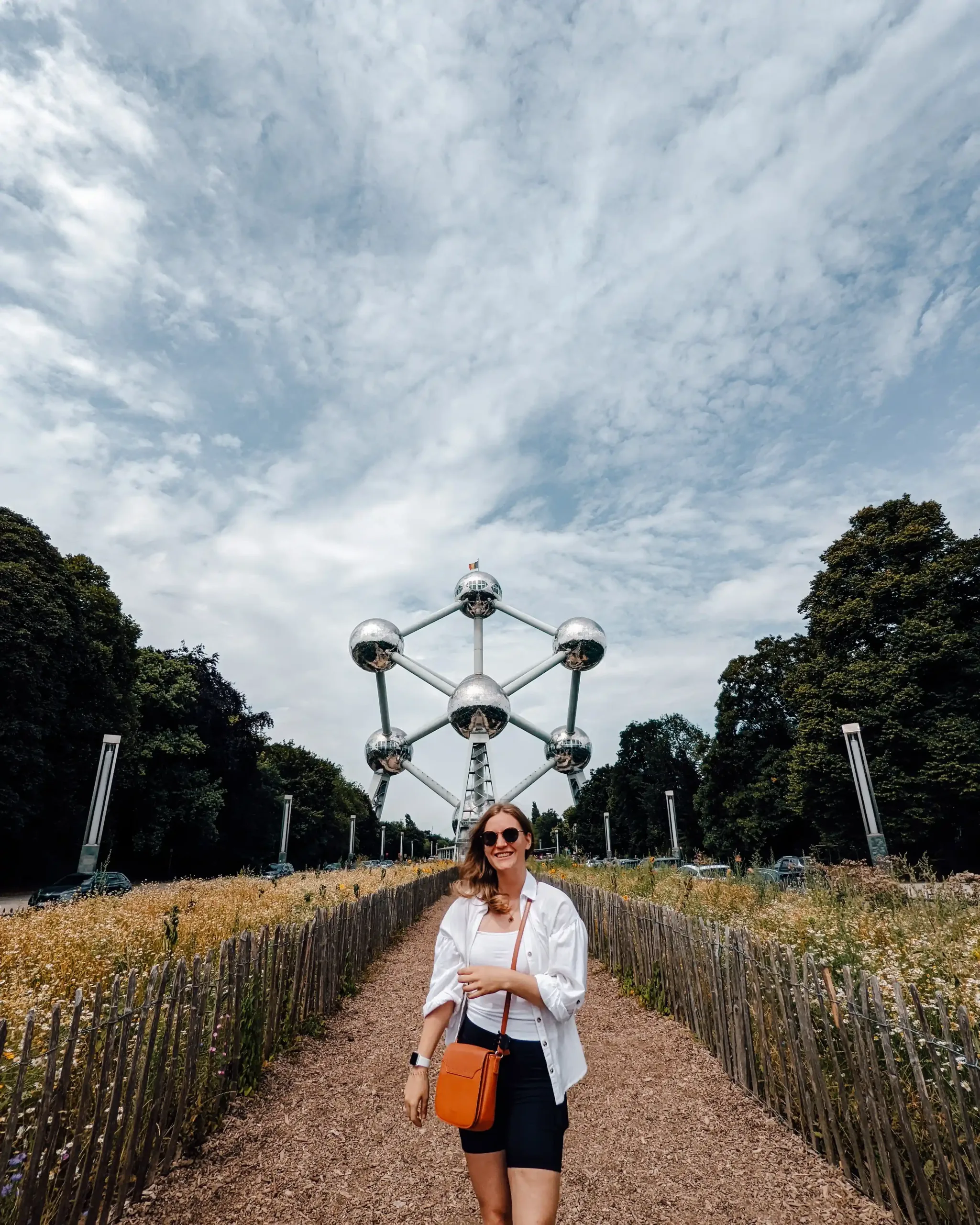 A girl standing on a dirt road leading up to the large, metalic Atomium statue in the background 