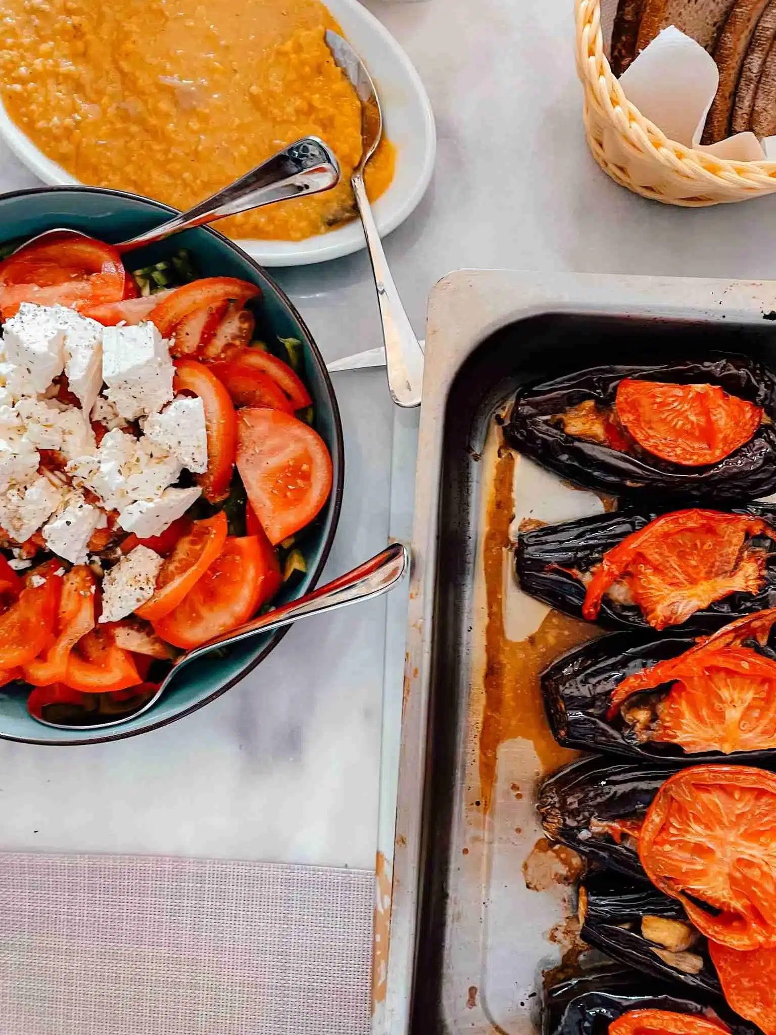 A table full of delicious, vibrant homemade Greek food made during a cooking class including a salad topped with bright tomatoes and feta cheese, eggplants stuffed with tomatoes and veggies.