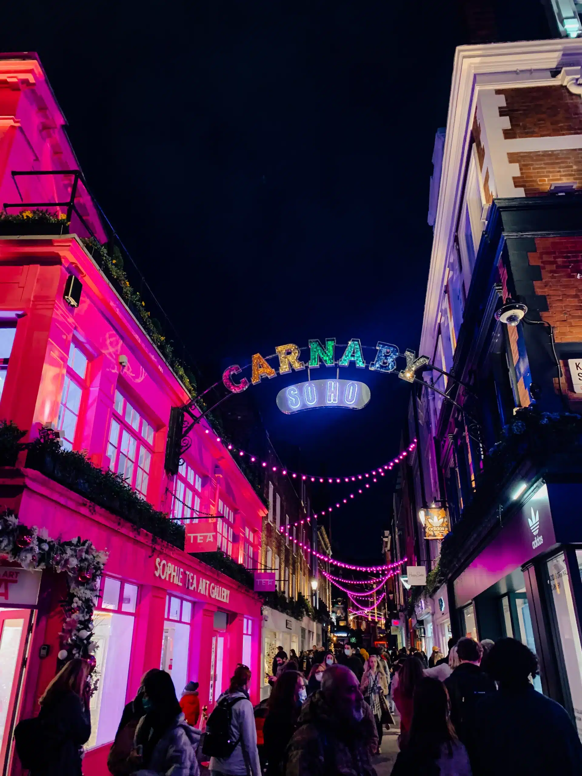 A busy, bright Carnaby Street in London, covered with colorful Christmas lights
