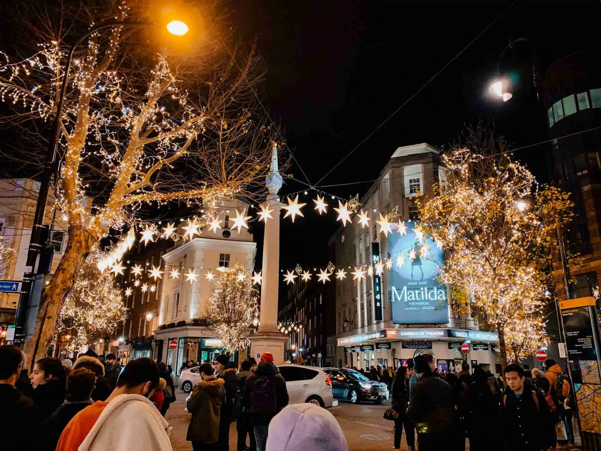 Twinkling Christmas lights in London light up the streets of Seven Dials, featuring star ornaments and lights hanging above the crowded streets