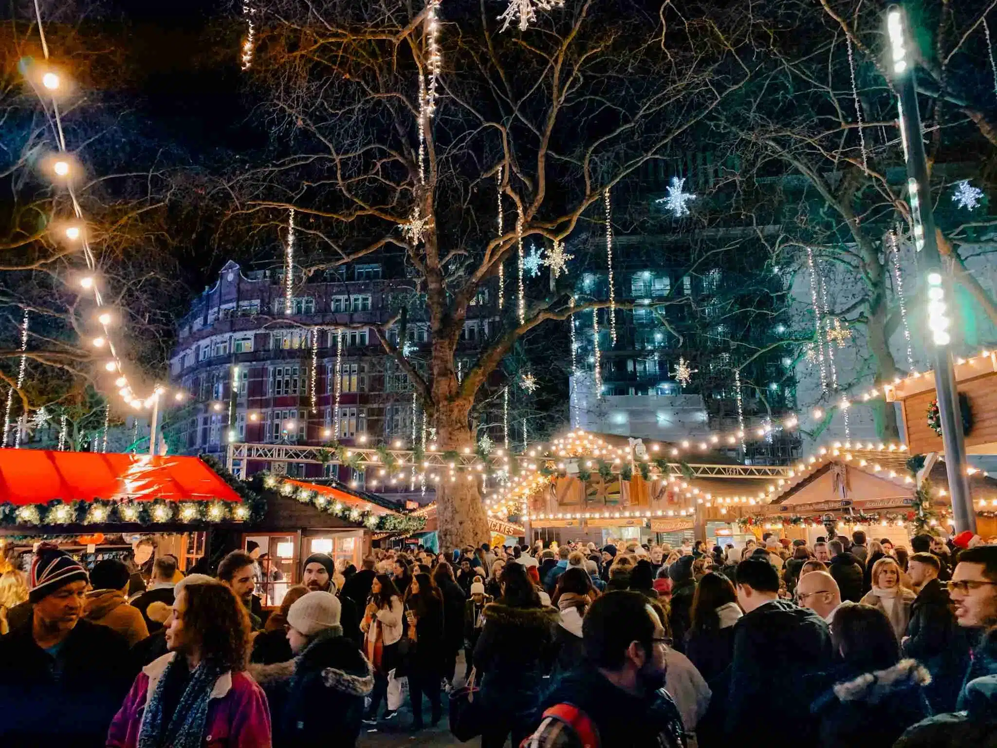 The busy Christmas market with twinkling lights and gingerbread-style booths in Leicester Square, London.