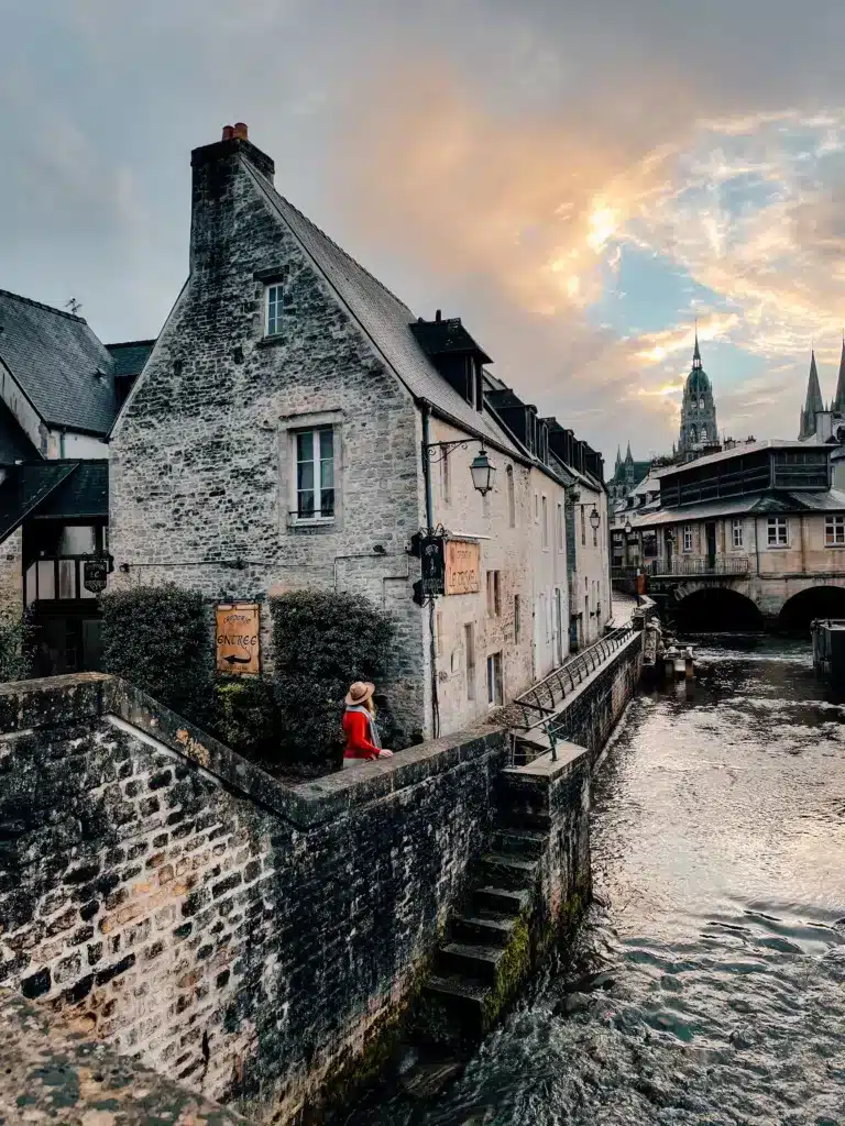A girl standing on a stone bridge overlooking a river passing through an old medieval town