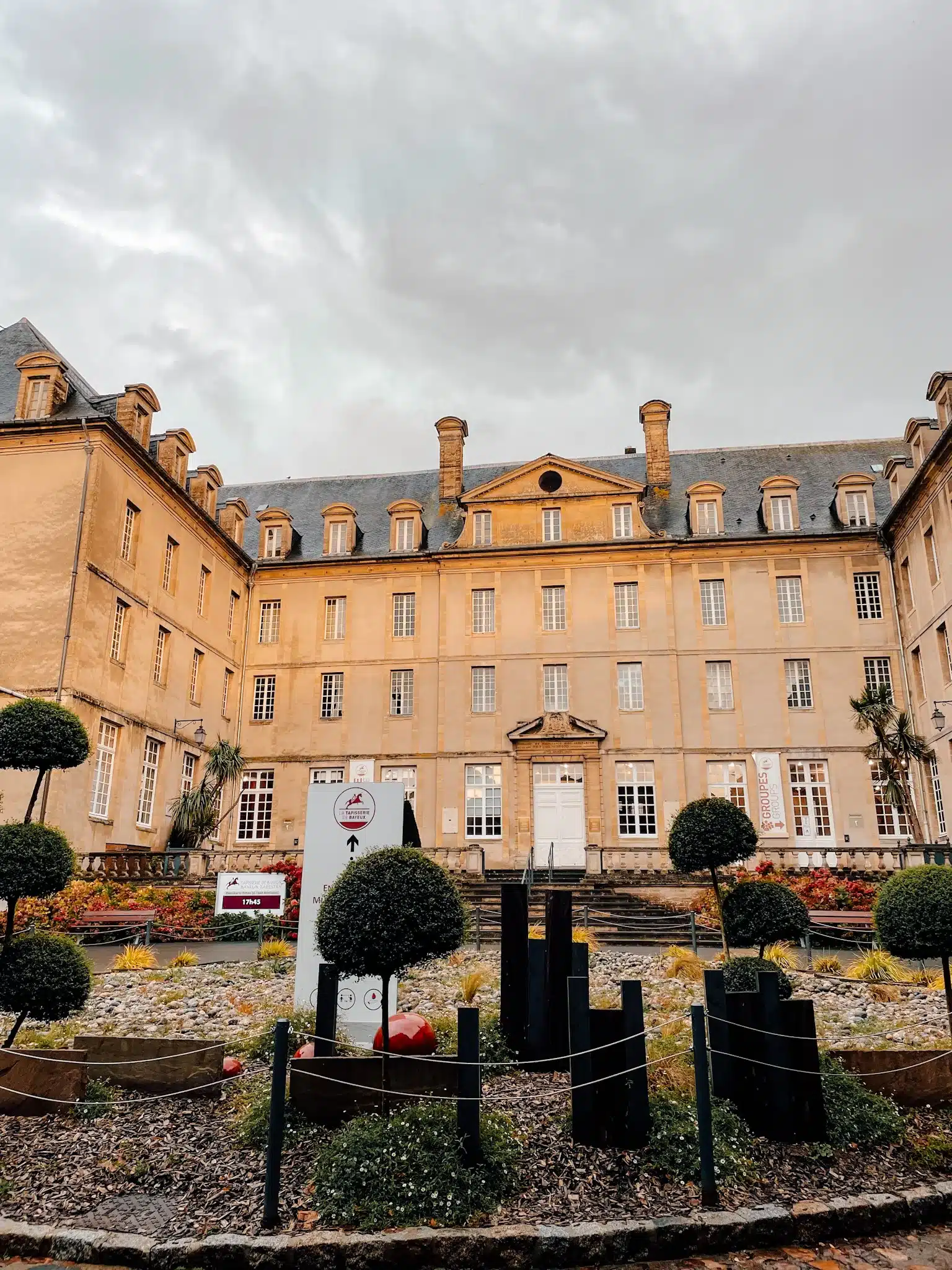 The front of the Bayeux Tapestry museum with a gardens of plants in the foreground and a large french building in the background