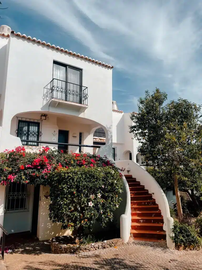 A beautiful white house with a staircase leading up to the second floor and a full garden in front.
