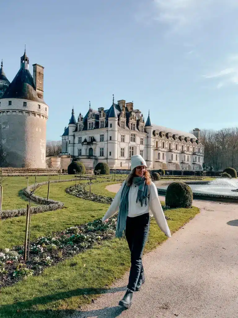 A girl walking through the gardens in front of a beautiful white castle